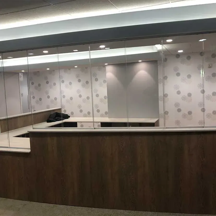 A wooden reception desk stands in front of a glass partition against a wall with a light-colored polka dot pattern.