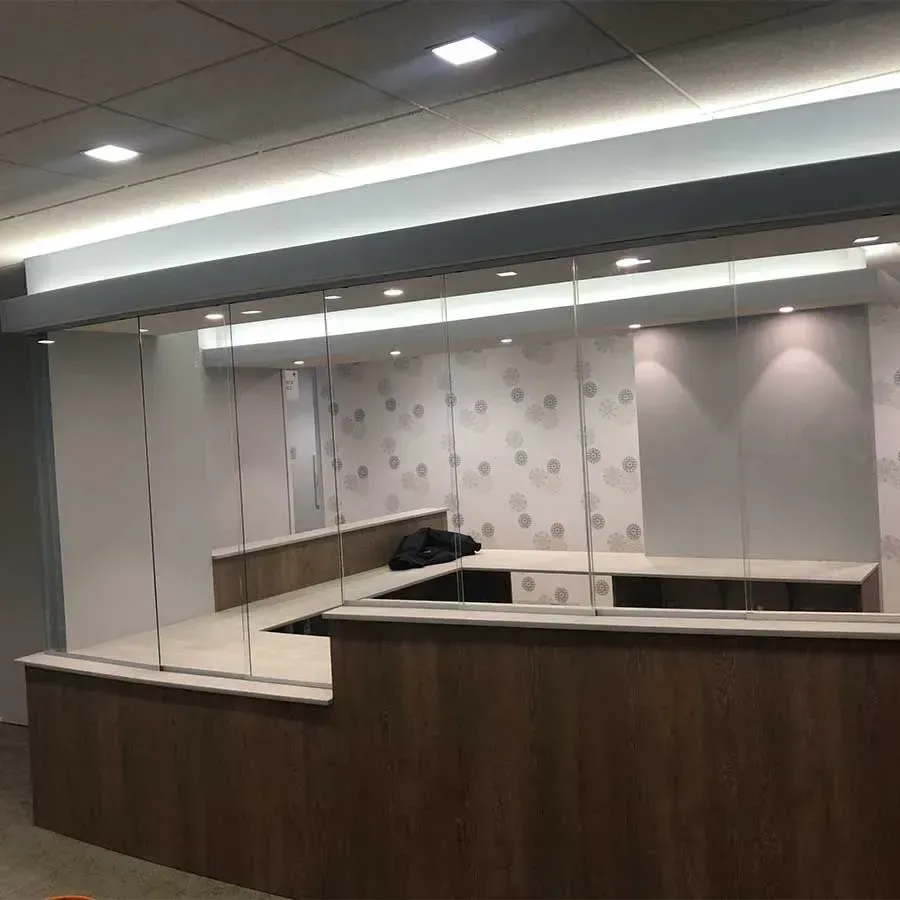 A reception desk with wood-grain panels and a glass partition in an office setting with patterned and solid gray walls.