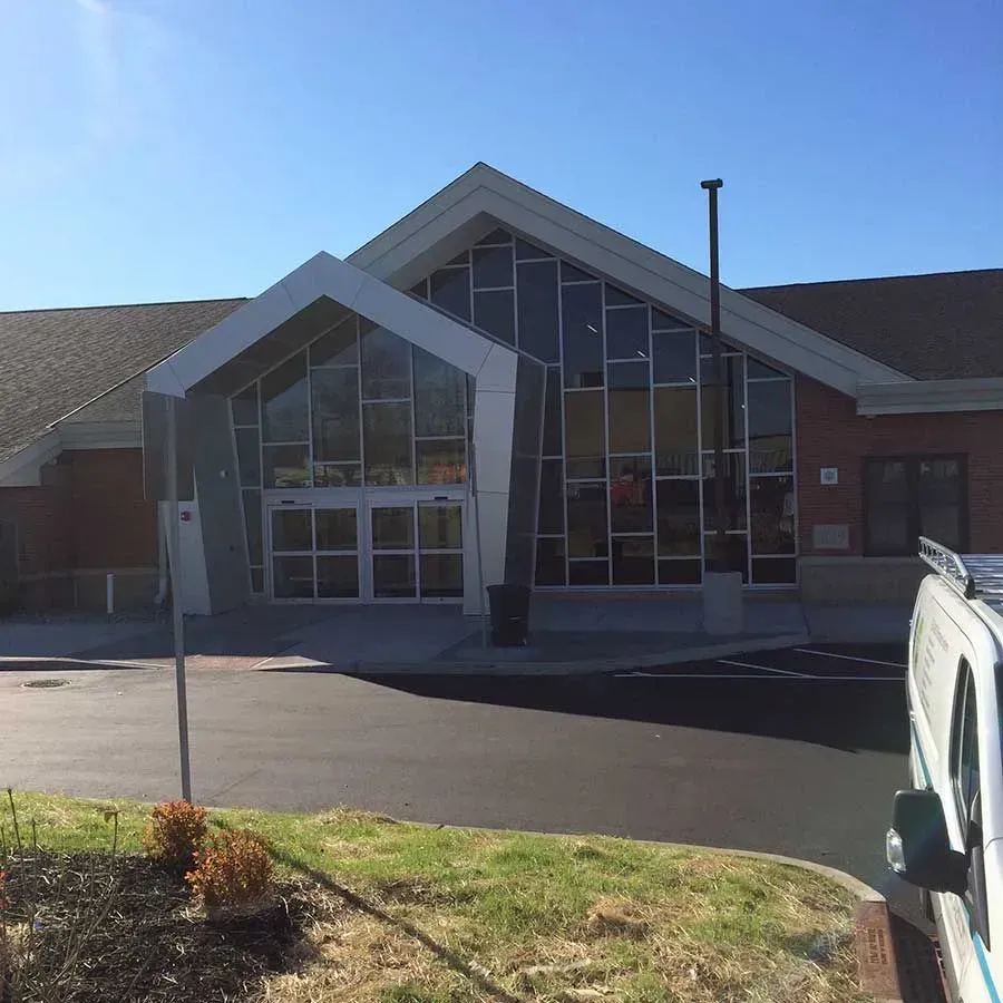 A brick building entrance with a geometric glass facade and a prominent peaked doorway under a bright blue sky.