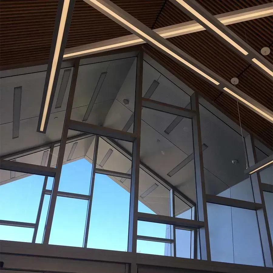 A modern, angular indoor space featuring a large glass window pane set in a gray frame with slatted wood ceilings.