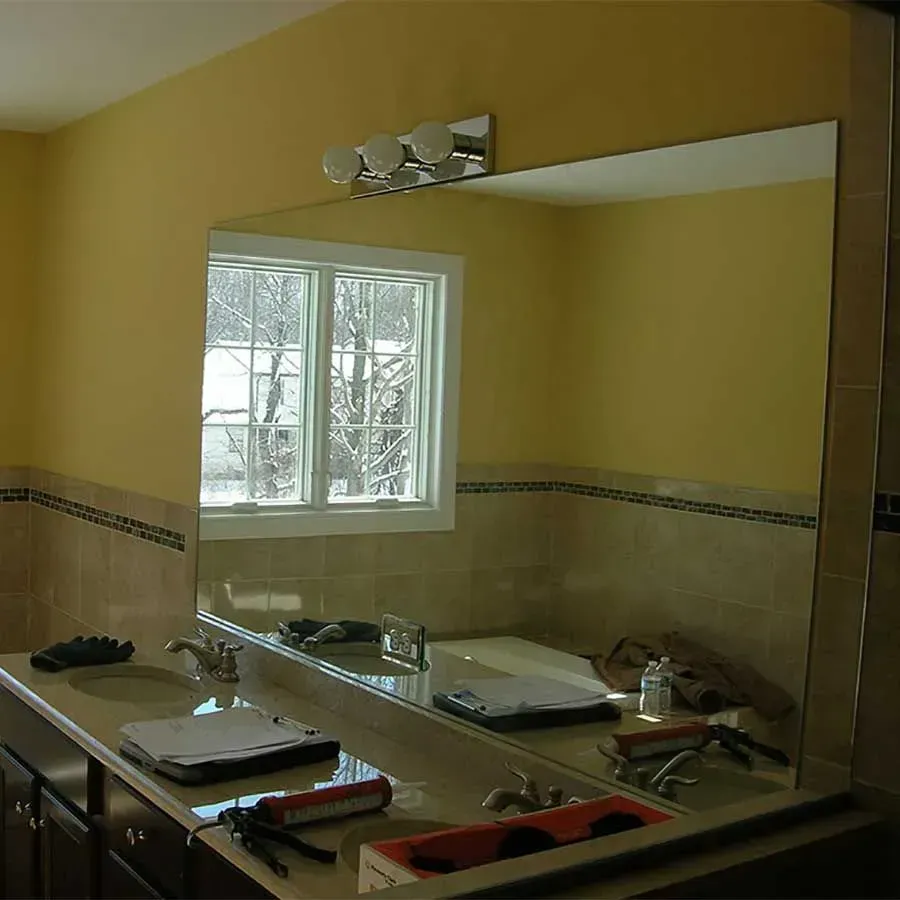 Bathroom vanity with a large mirror, yellow walls, tiled backsplash, and construction tools on the counter.