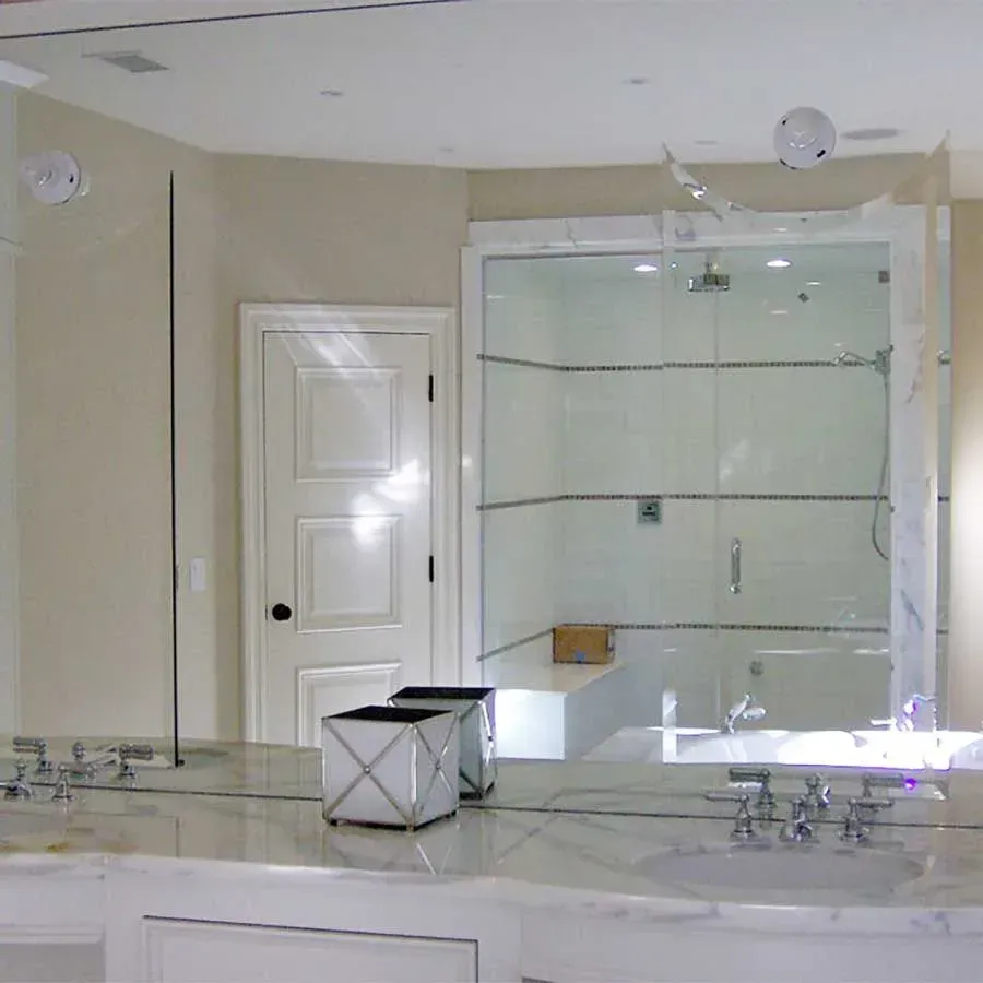 A modern bathroom with a double vanity, marble countertops, a large mirror, and a glass-enclosed shower with a seat.