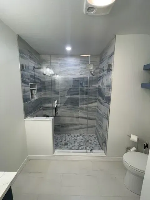 A modern bathroom featuring a walk-in shower with gray marbled tile walls and a pebble-tiled floor behind a glass door.