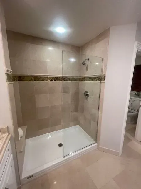 A walk-in shower with a glass door, beige tiled walls, a decorative horizontal accent border, and a white shower floor.