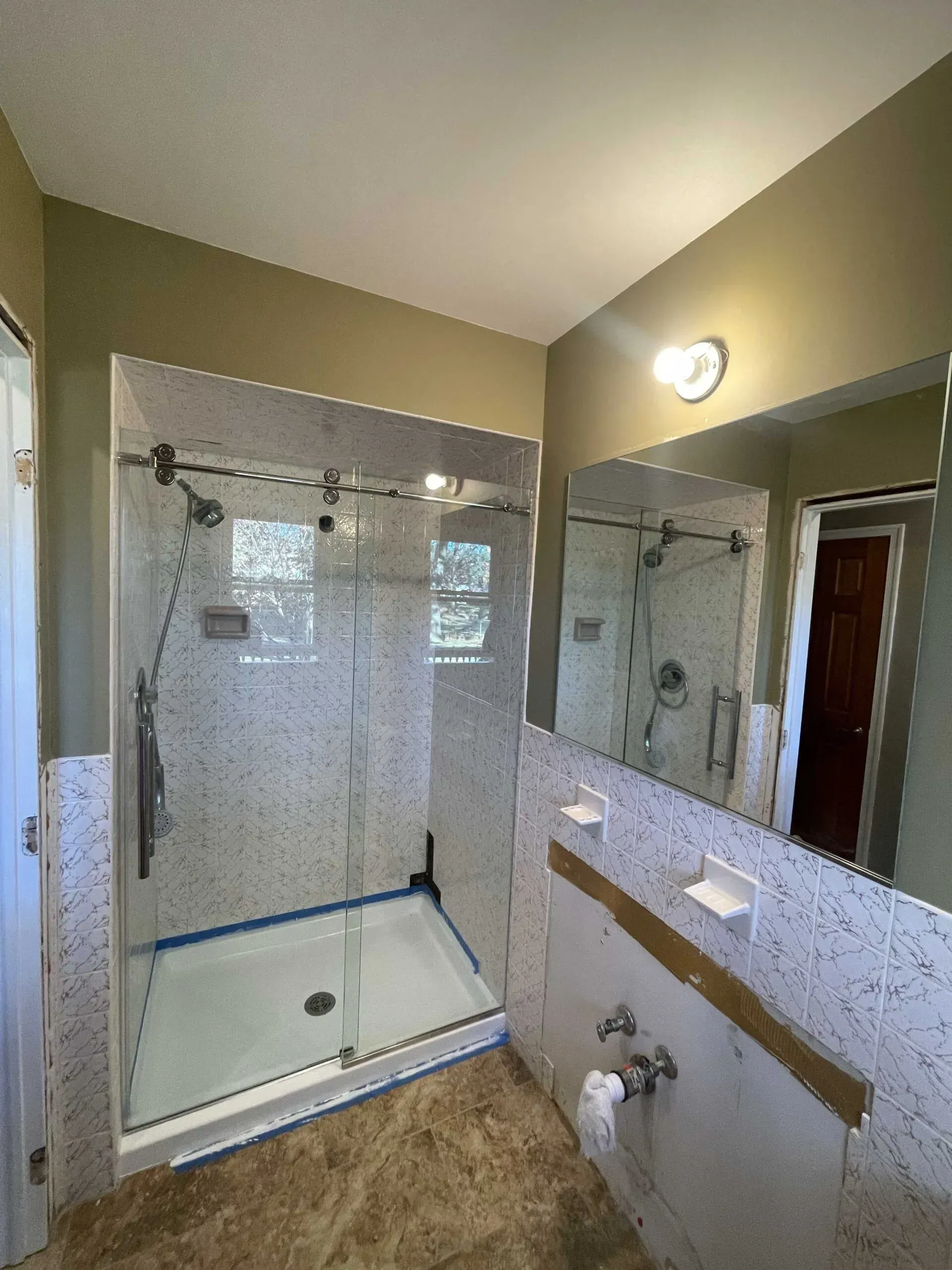 A modern bathroom featuring a glass shower stall, a large mirror over an unfinished vanity, and neutral-toned tiled walls.