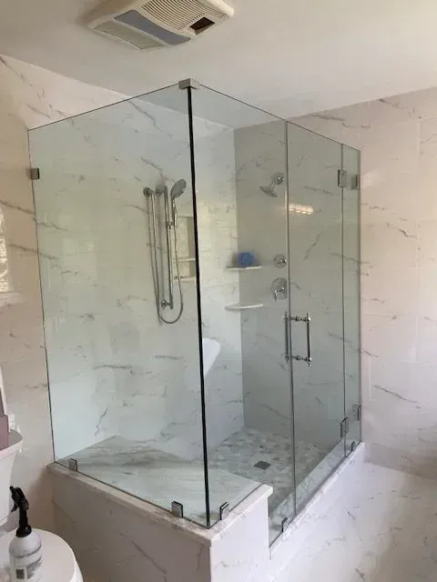 A glass-enclosed shower with marble-patterned tiles and stone floor in a modern bathroom.