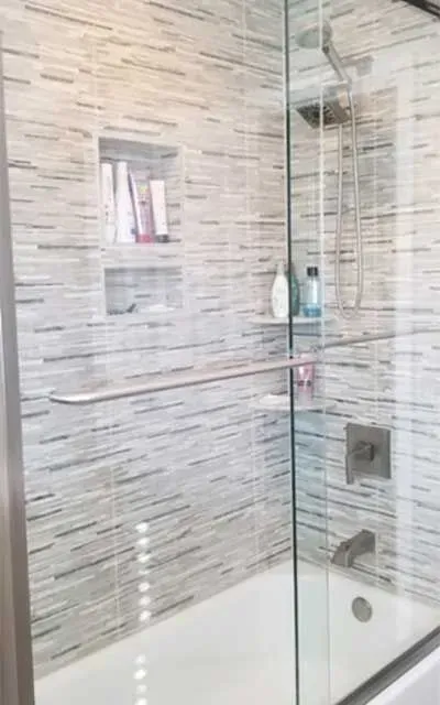 A tiled walk-in shower with a glass door, built-in shelving niches, a chrome showerhead, and a bathtub.