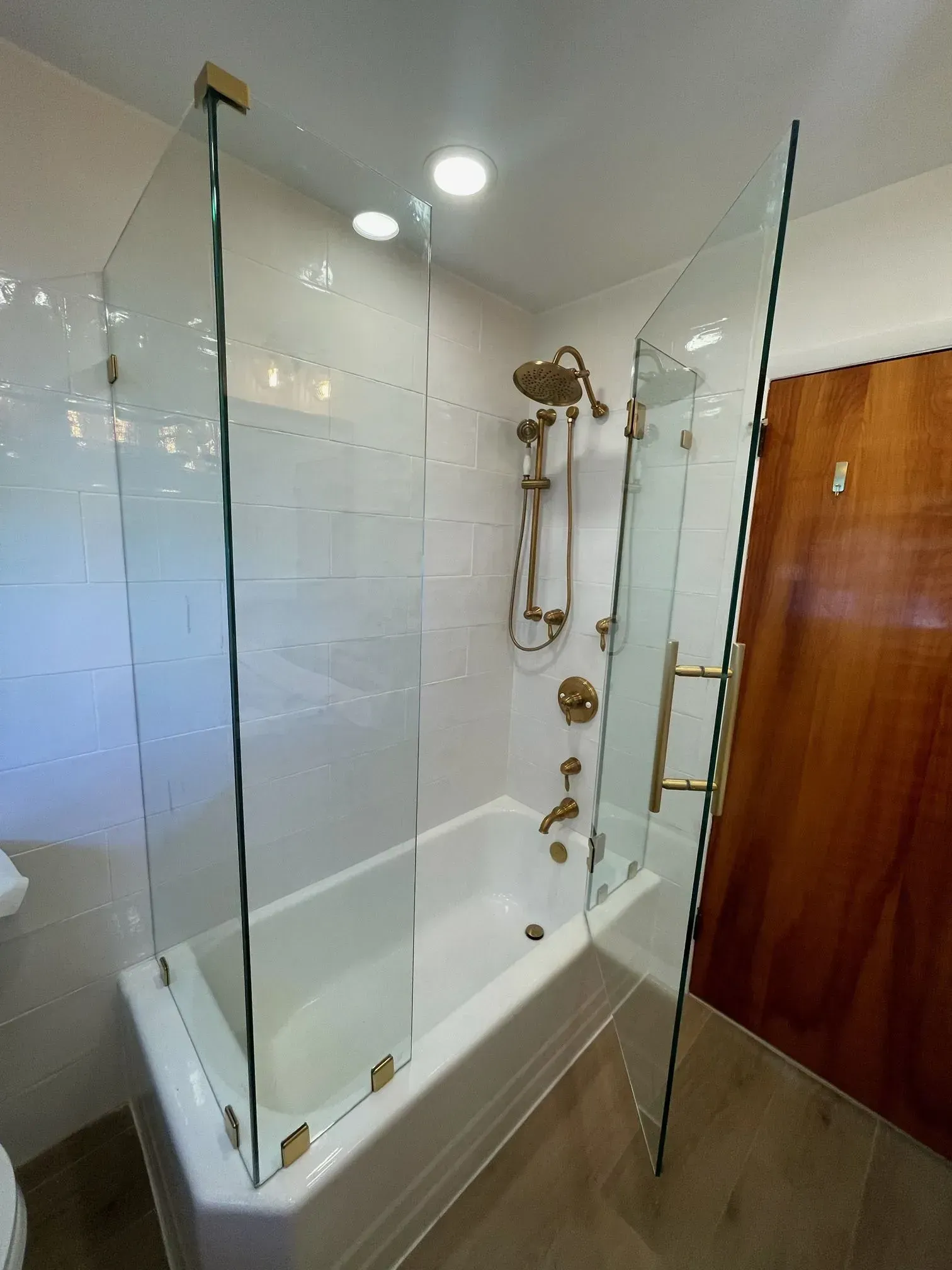 A bathtub with a glass shower screen and gold hardware, featuring a wall-mounted shower head and faucet.