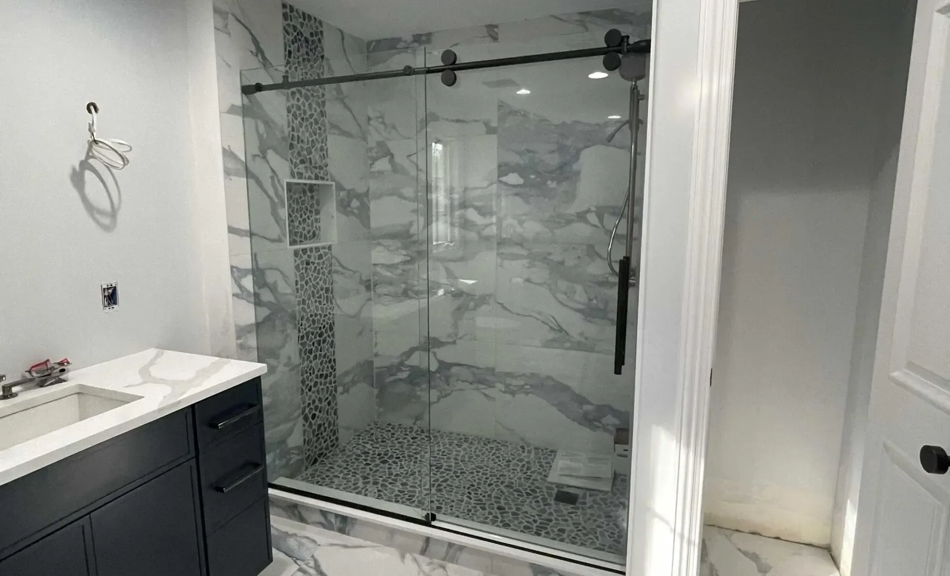A modern bathroom featuring a black vanity with a white countertop next to a glass walk-in shower with marble tile walls.
