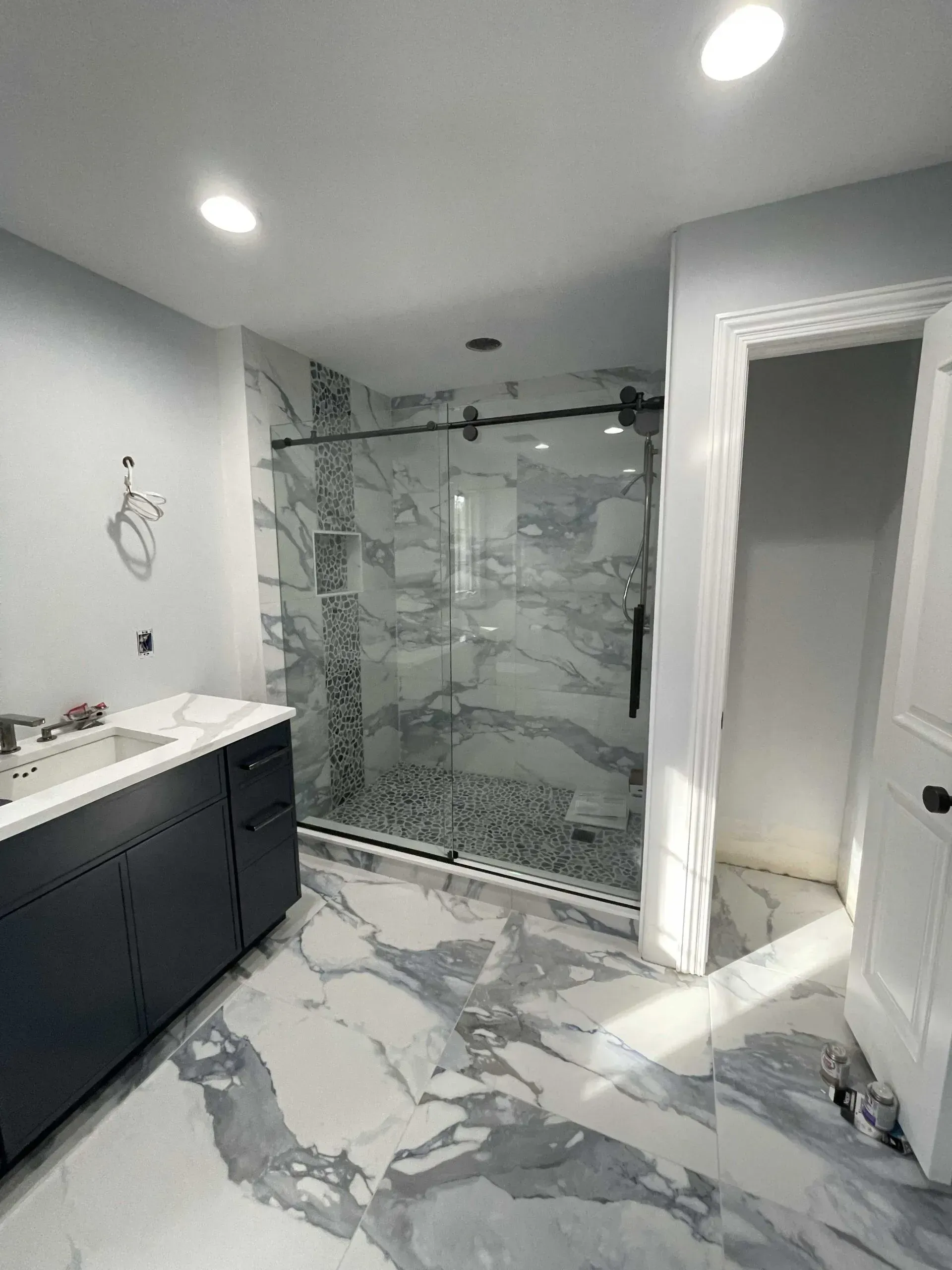 Modern bathroom featuring a dark vanity, marble-style floor tiles, a glass-enclosed shower, and a doorway to a closet.