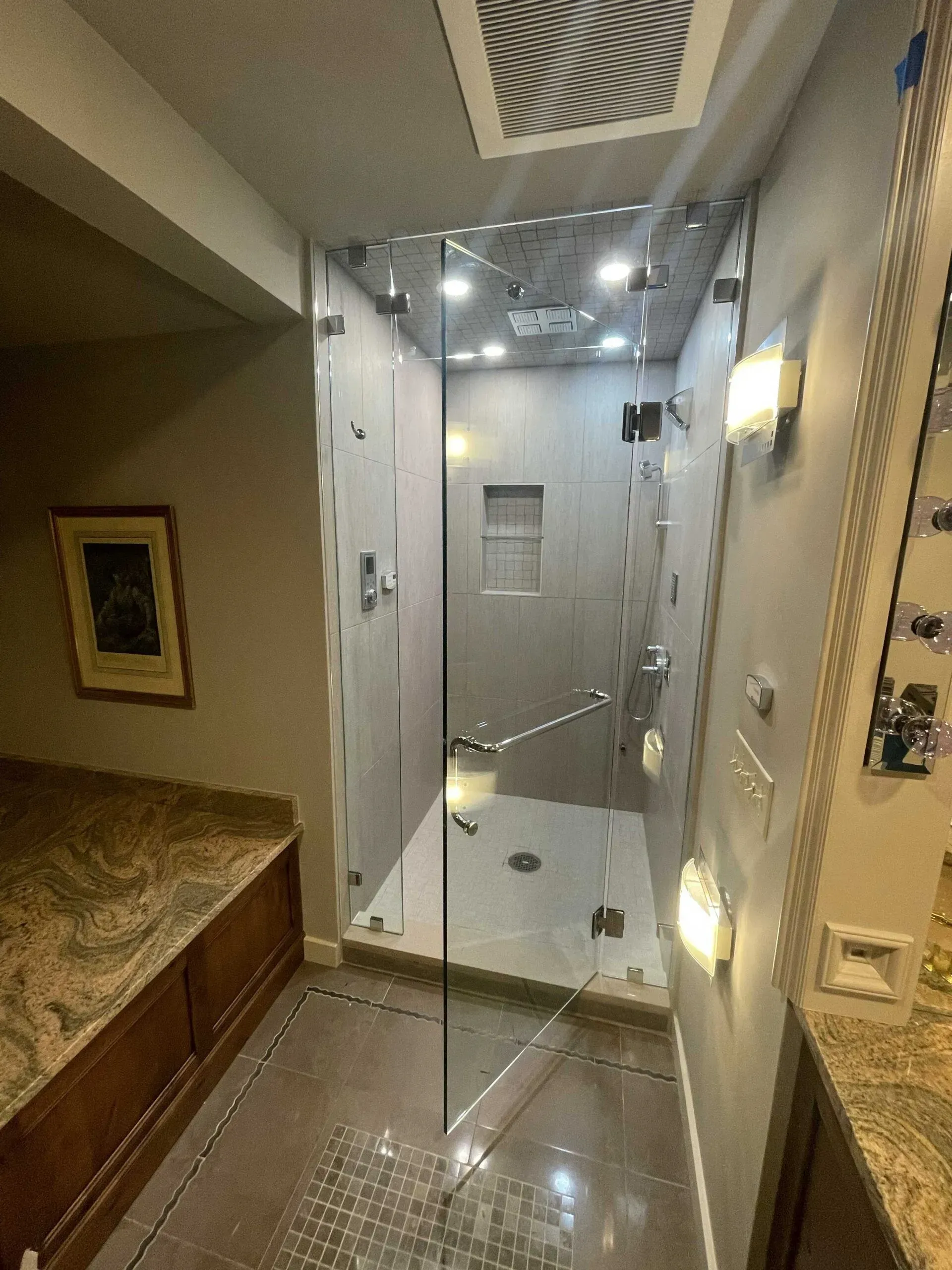 A tiled walk-in shower with a glass door in a bathroom with granite counters and recessed ceiling lighting.