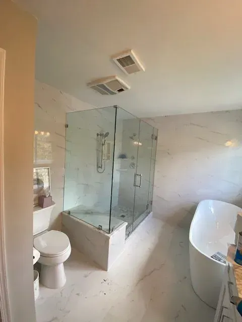 A modern bathroom with a glass-enclosed shower, a white soaking tub, and a toilet against white marble-tiled walls.