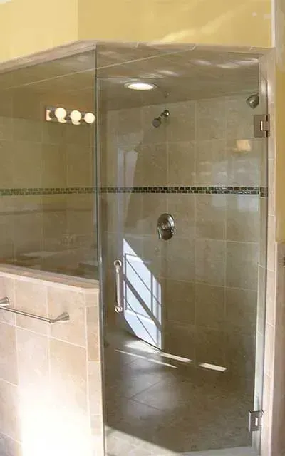 A walk-in shower with beige tile walls, a glass door, and a horizontal grab bar mounted on an exterior tiled half-wall.