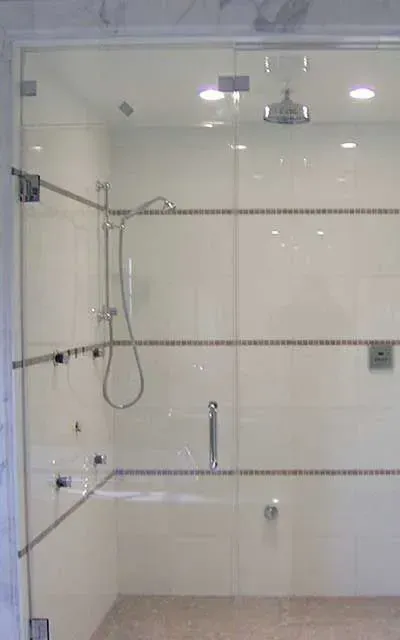 A frameless glass shower enclosure featuring white subway tile walls with decorative horizontal accents and chrome fixtures.