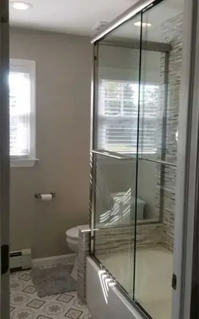 A bathroom featuring a tiled floor, gray walls, a toilet, and a glass-enclosed shower with a stone-look tiled wall.