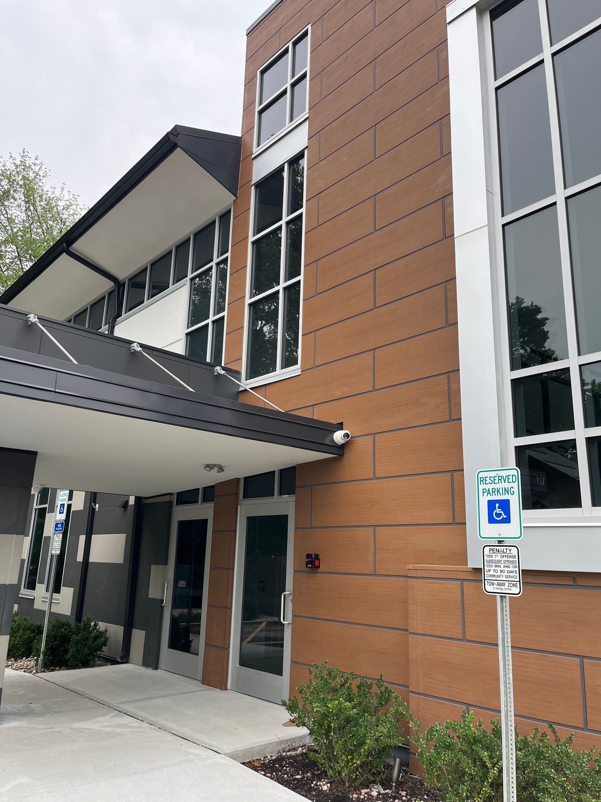 Modern building entrance with orange brick facade, glass windows, and an accessible parking sign by the doorway