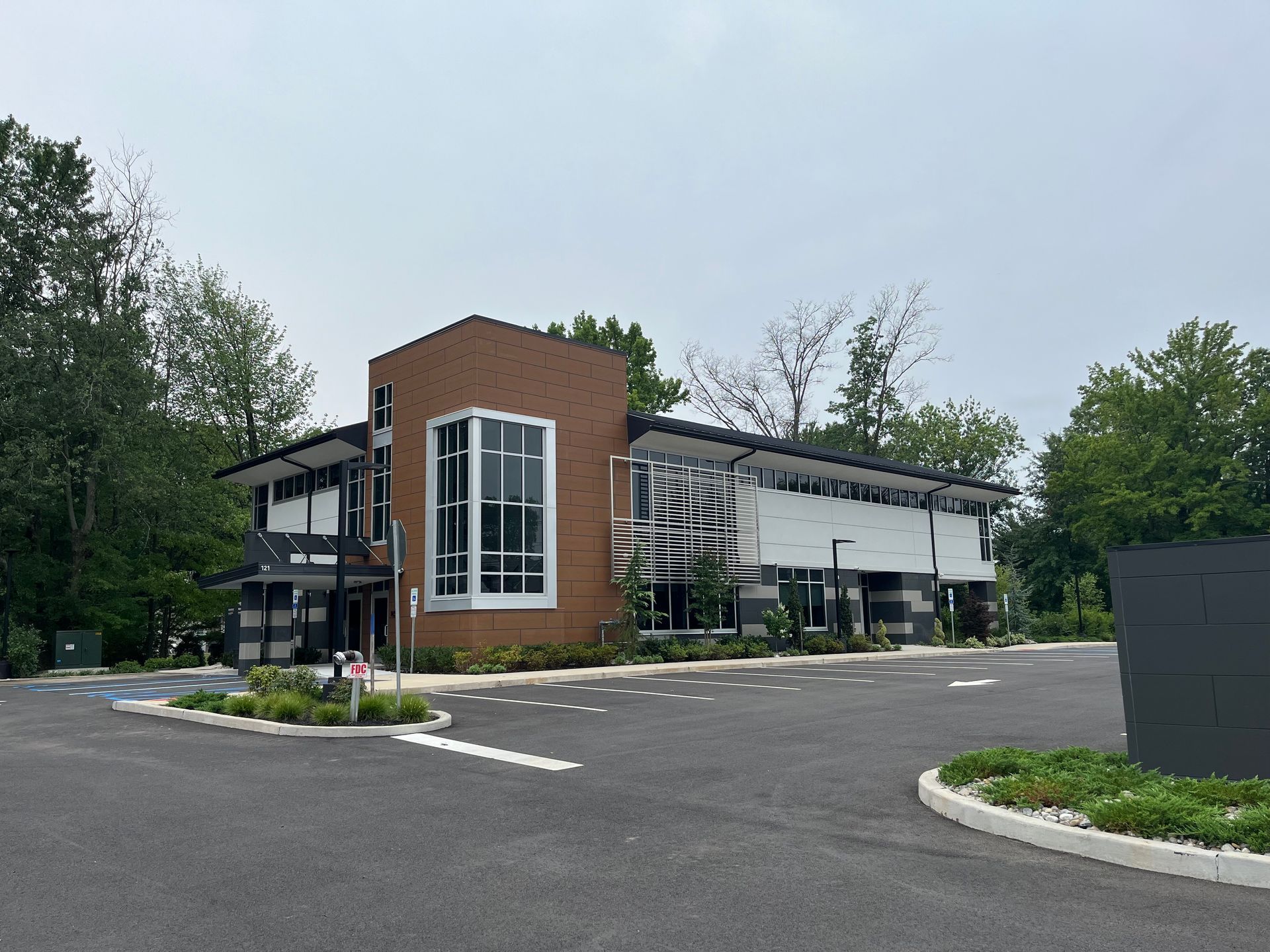 Modern building with brick tower, glass entrance, and empty parking lot surrounded by trees