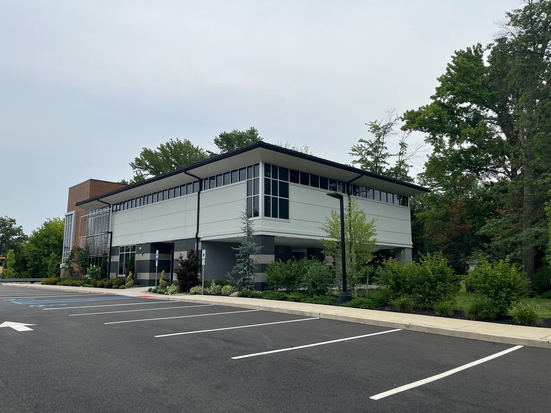 Modern two-story building with white siding beside an empty parking lot and trees