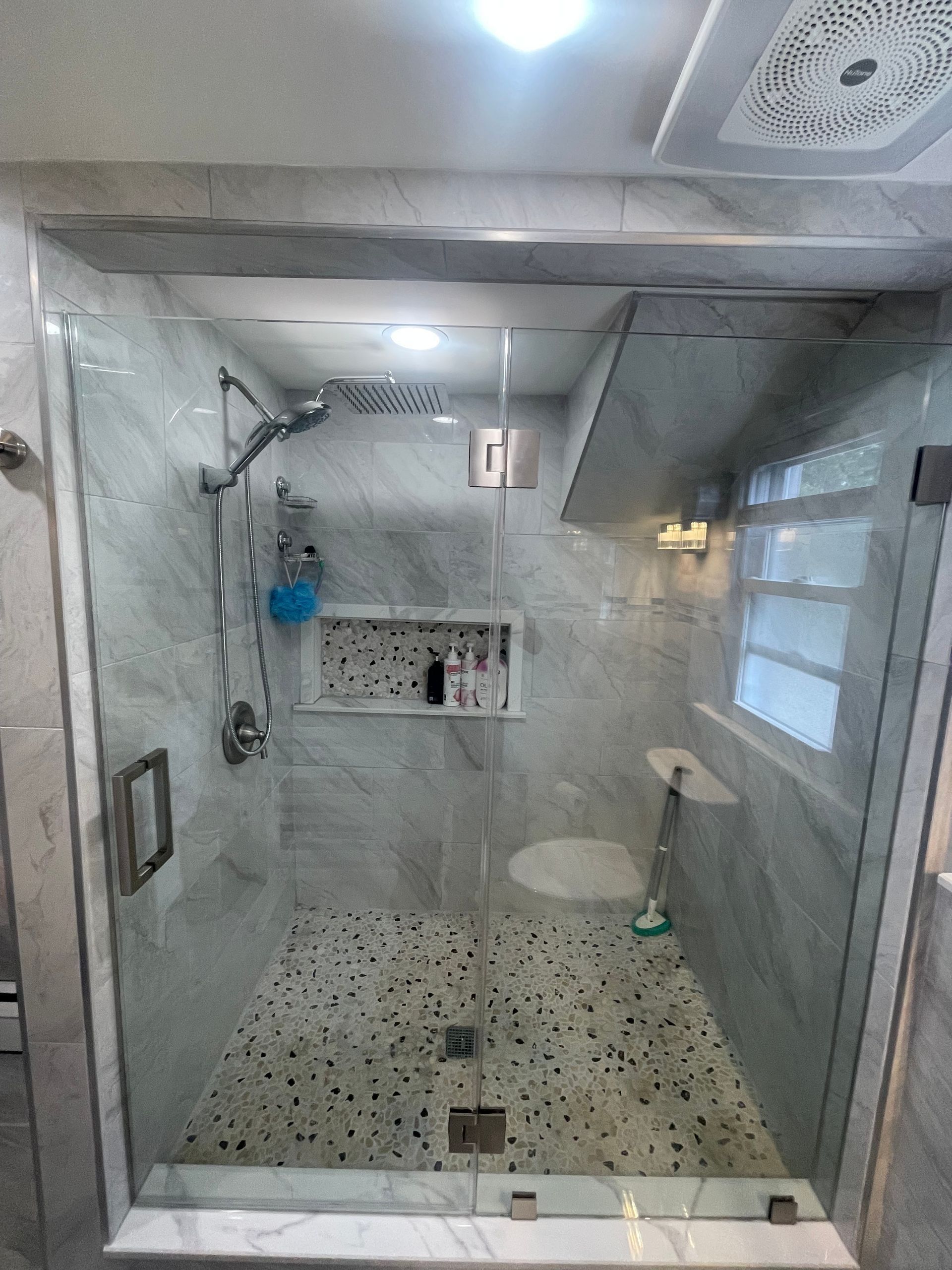 Modern tiled bathroom with glass shower enclosure, pebble floor, and windowed wall.