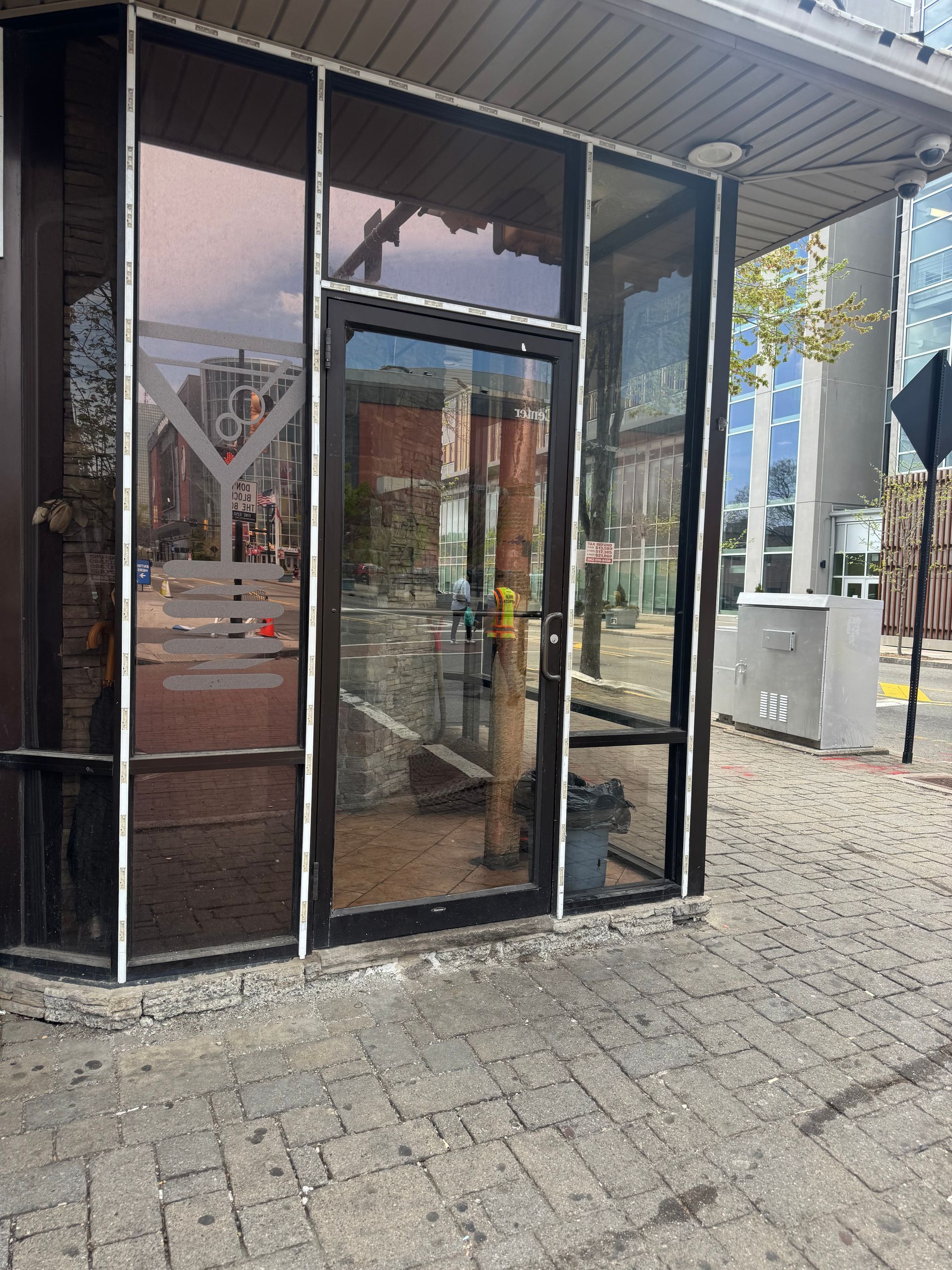 Small glass-front entrance pavilion with dark panels and a brick walkway outside