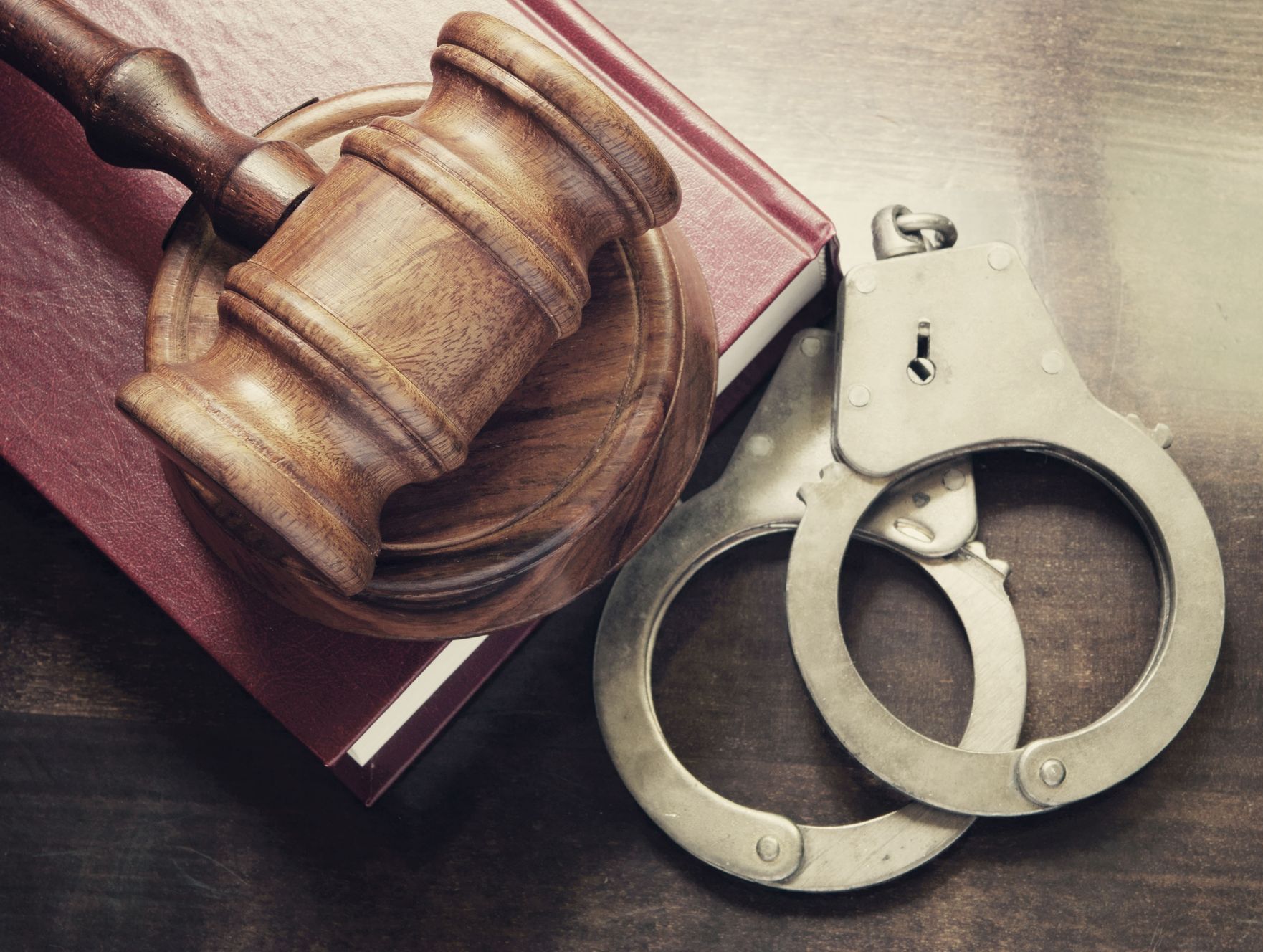 A wooden gavel and handcuffs are sitting on top of a book.