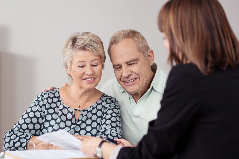 An elderly couple is sitting at a table talking to a woman.