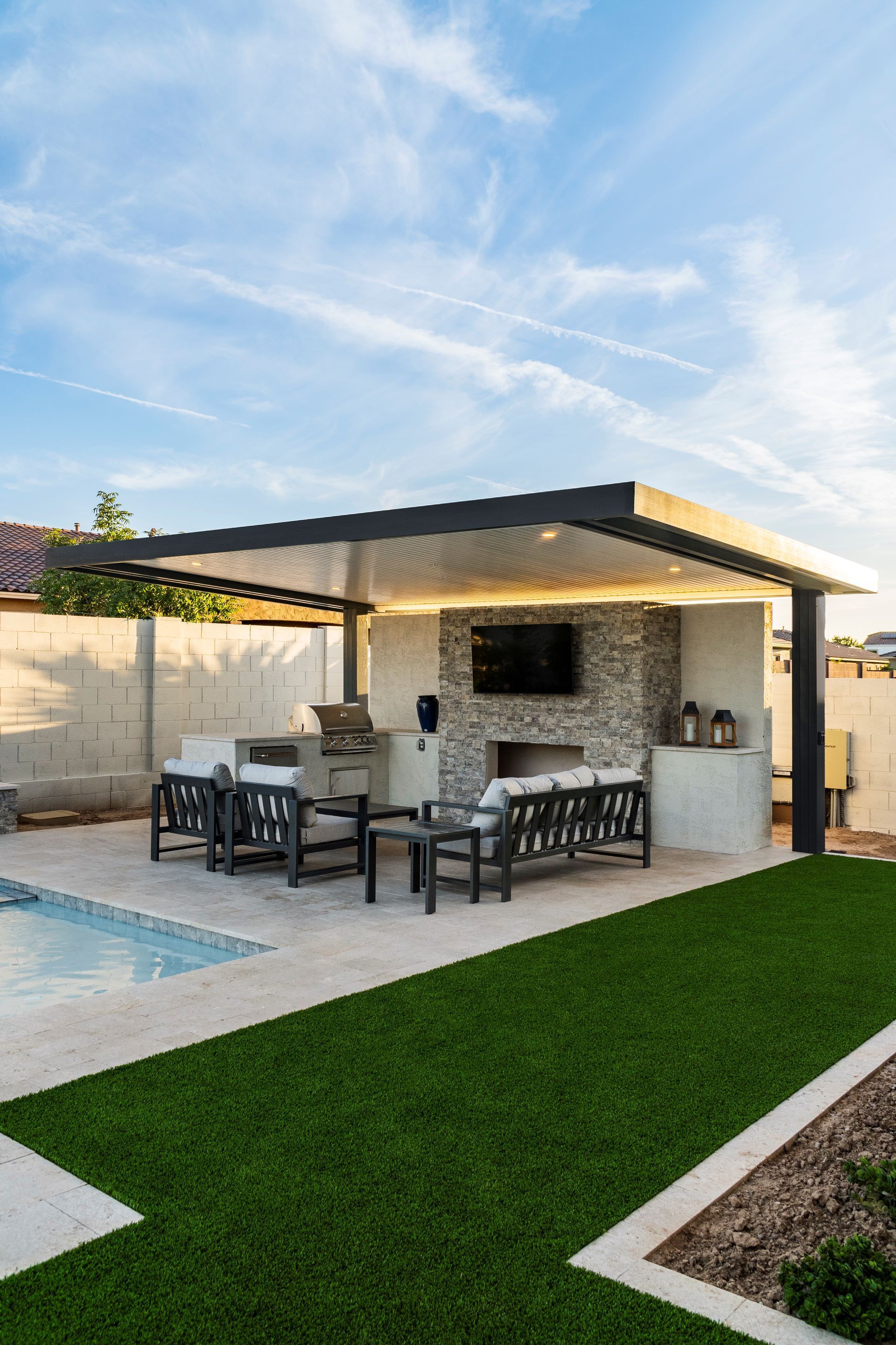 There is a pool in the backyard with a patio area and a fireplace.