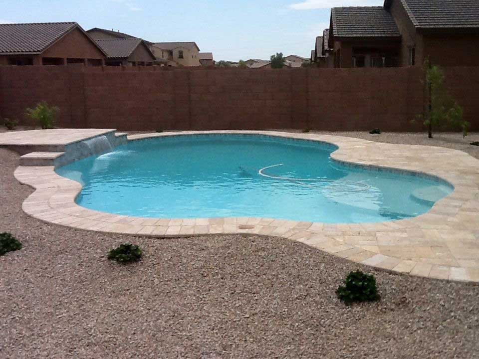 A large swimming pool is surrounded by gravel and a fence