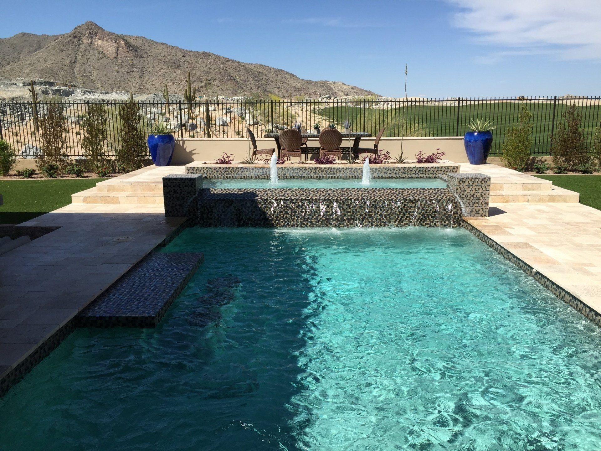 A large swimming pool with a waterfall and a table and chairs in the background.
