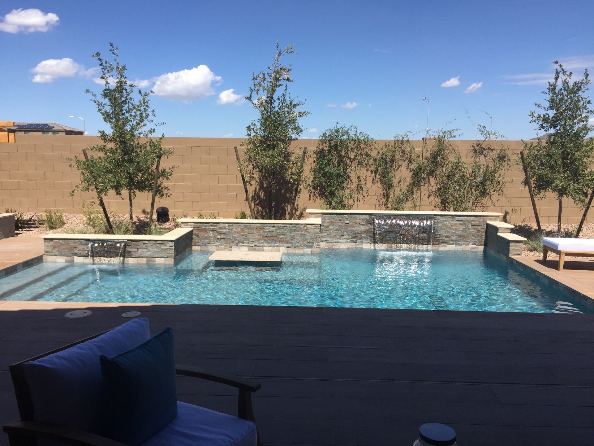 A large swimming pool is surrounded by trees and a chair.