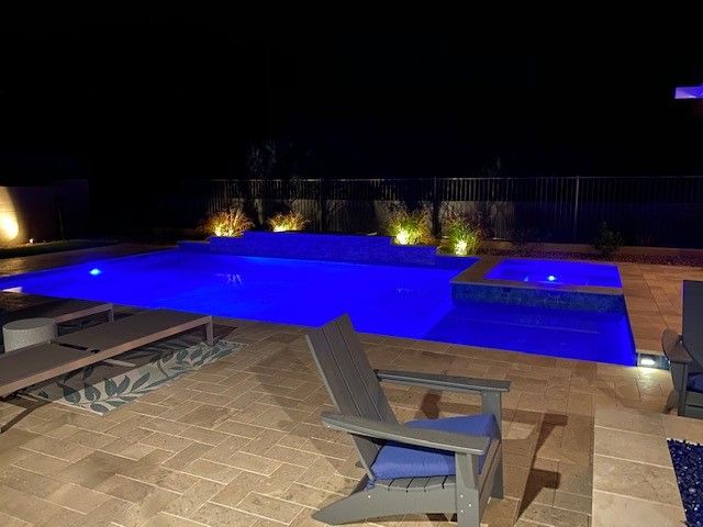 A large swimming pool is lit up at night with blue lights.