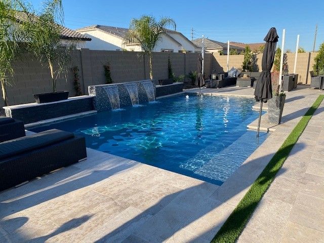 A large swimming pool is surrounded by gravel and a fence
