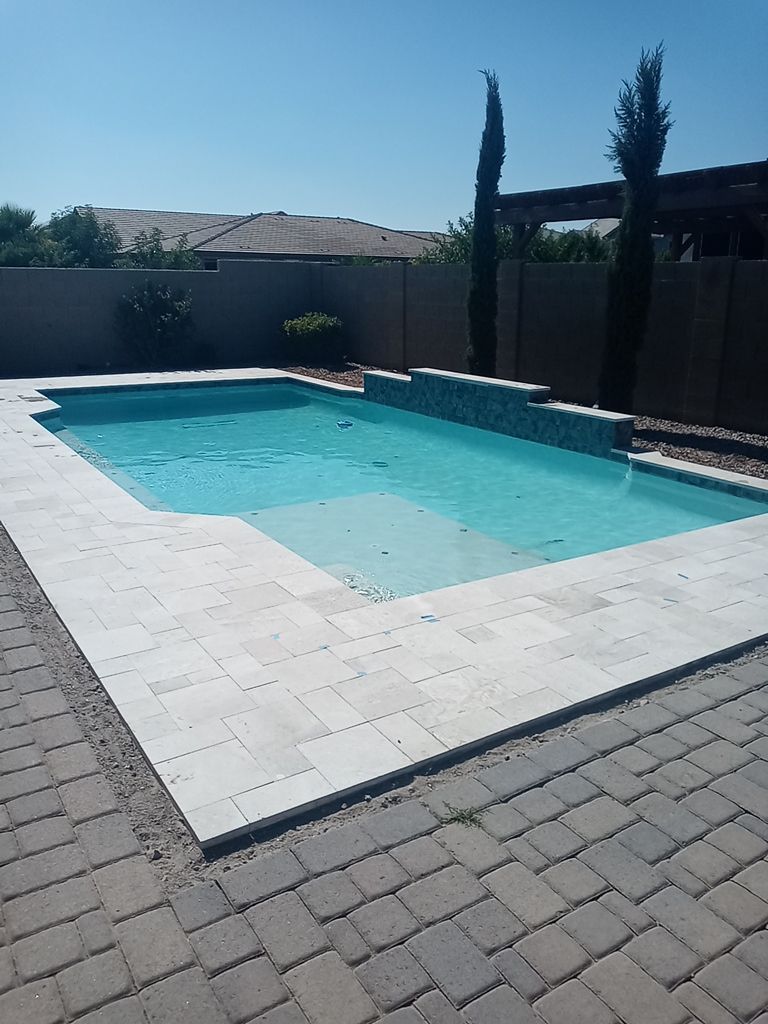 A large swimming pool is surrounded by a brick patio on a sunny day.