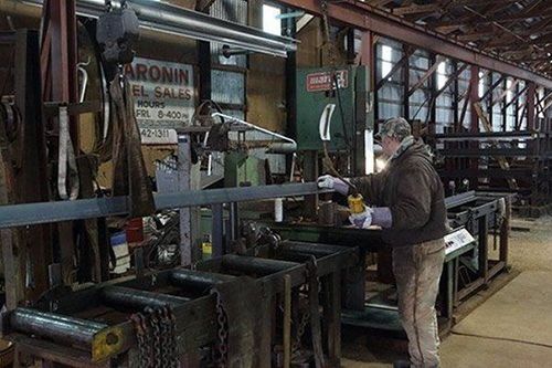 A person in a workshop working on a metal beam; they are wearing protective gear.