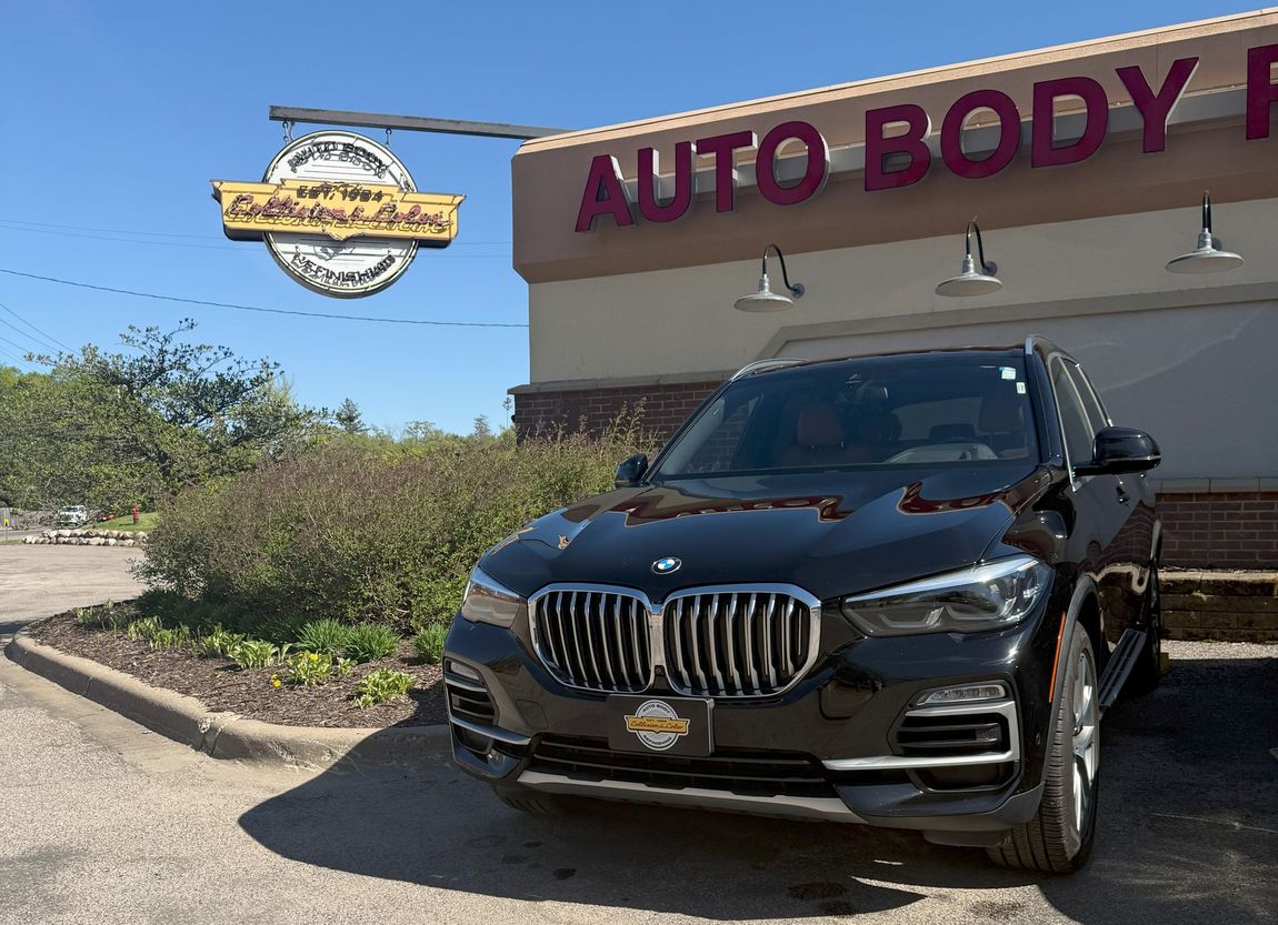 A black bmw is parked in front of an auto body shop