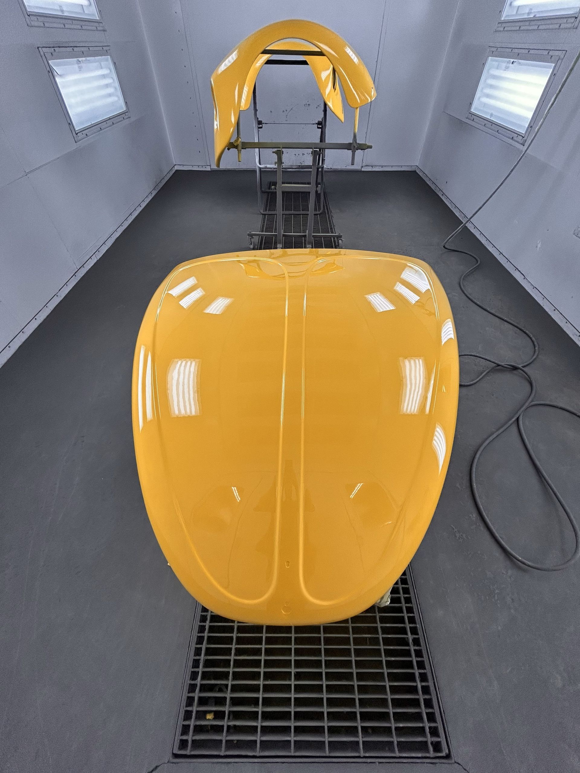 A yellow car is being painted in a paint booth