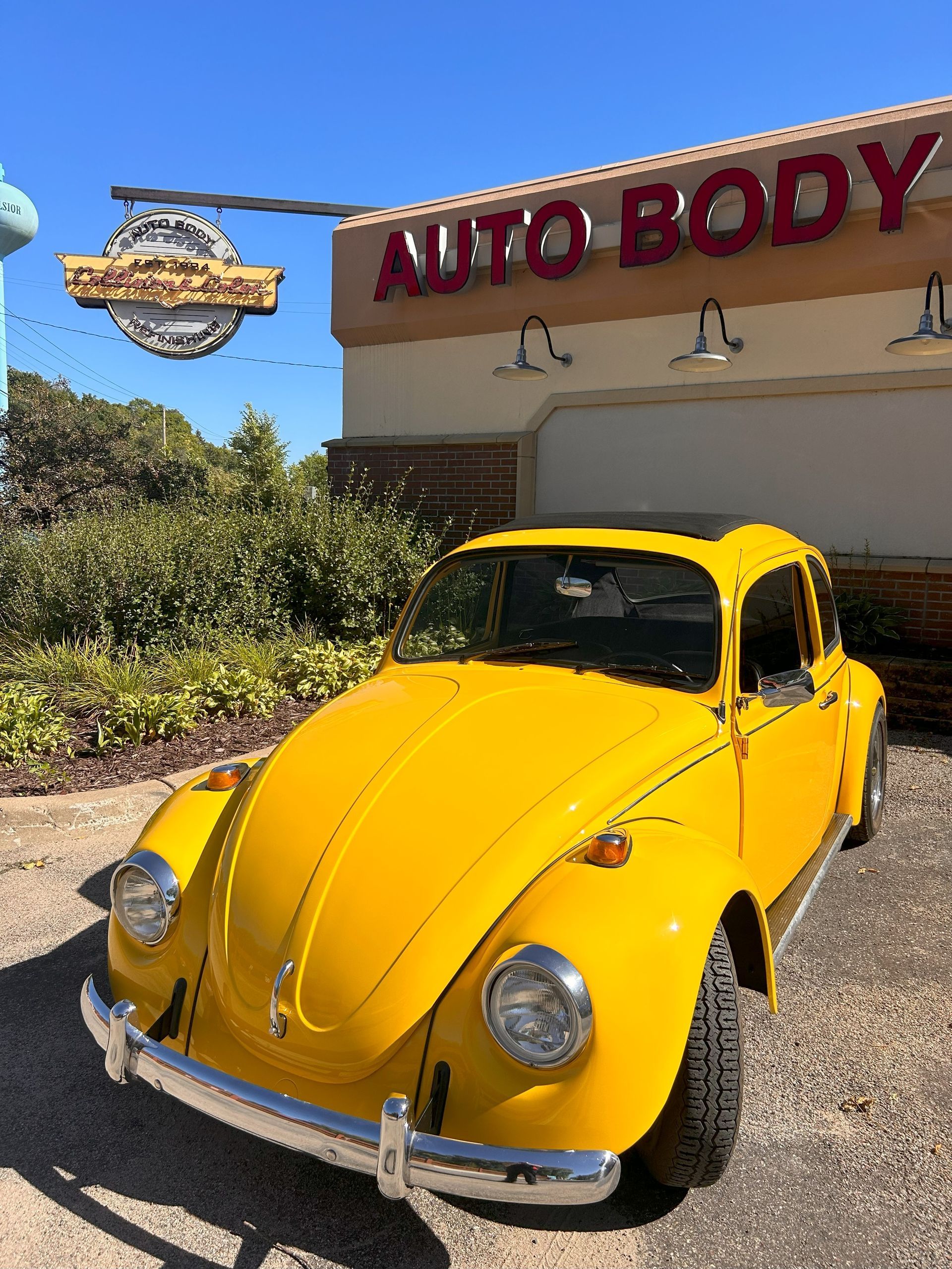 A yellow car is parked in front of an auto body shop