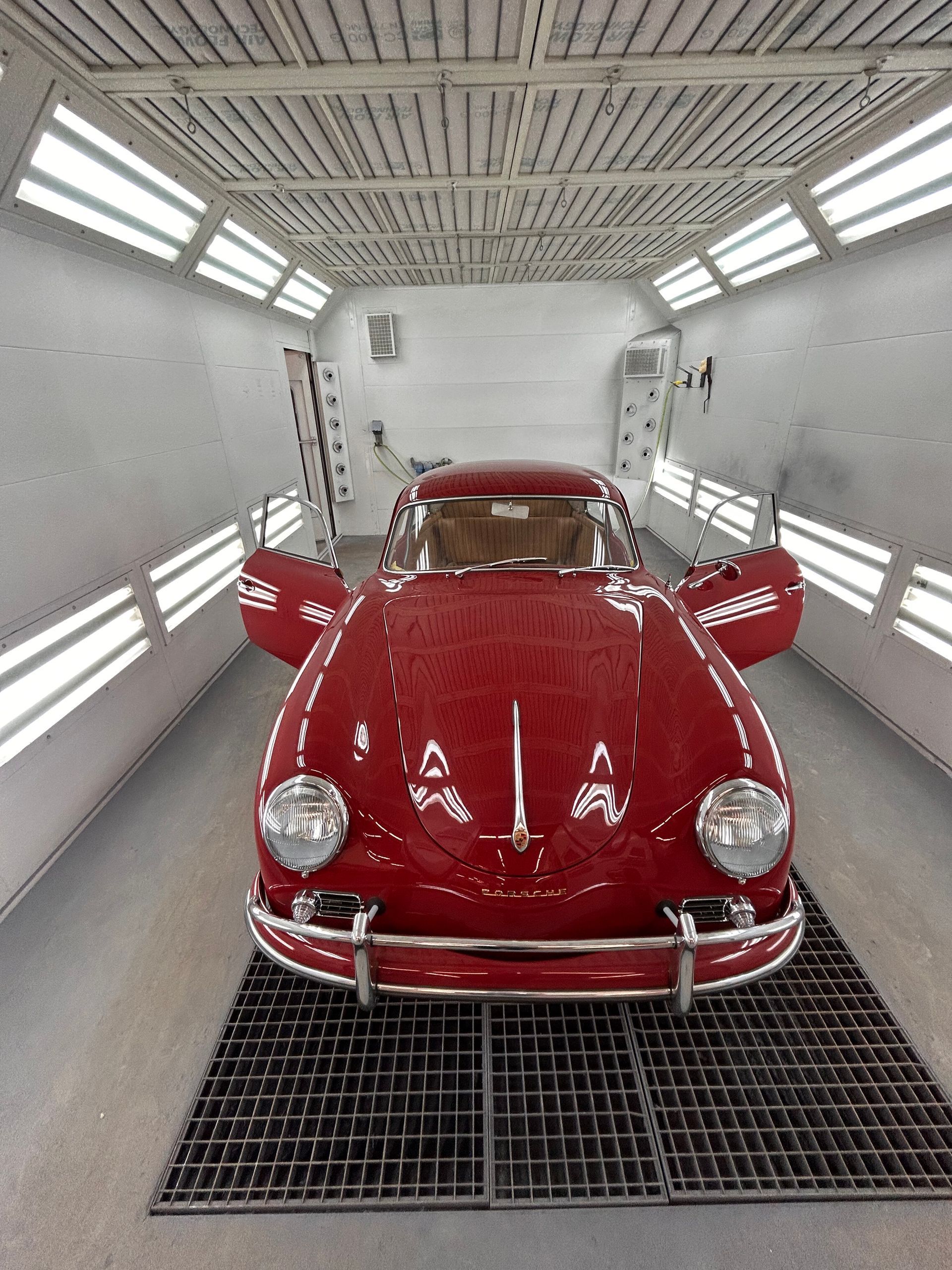 A red car is parked in a paint booth with its doors open