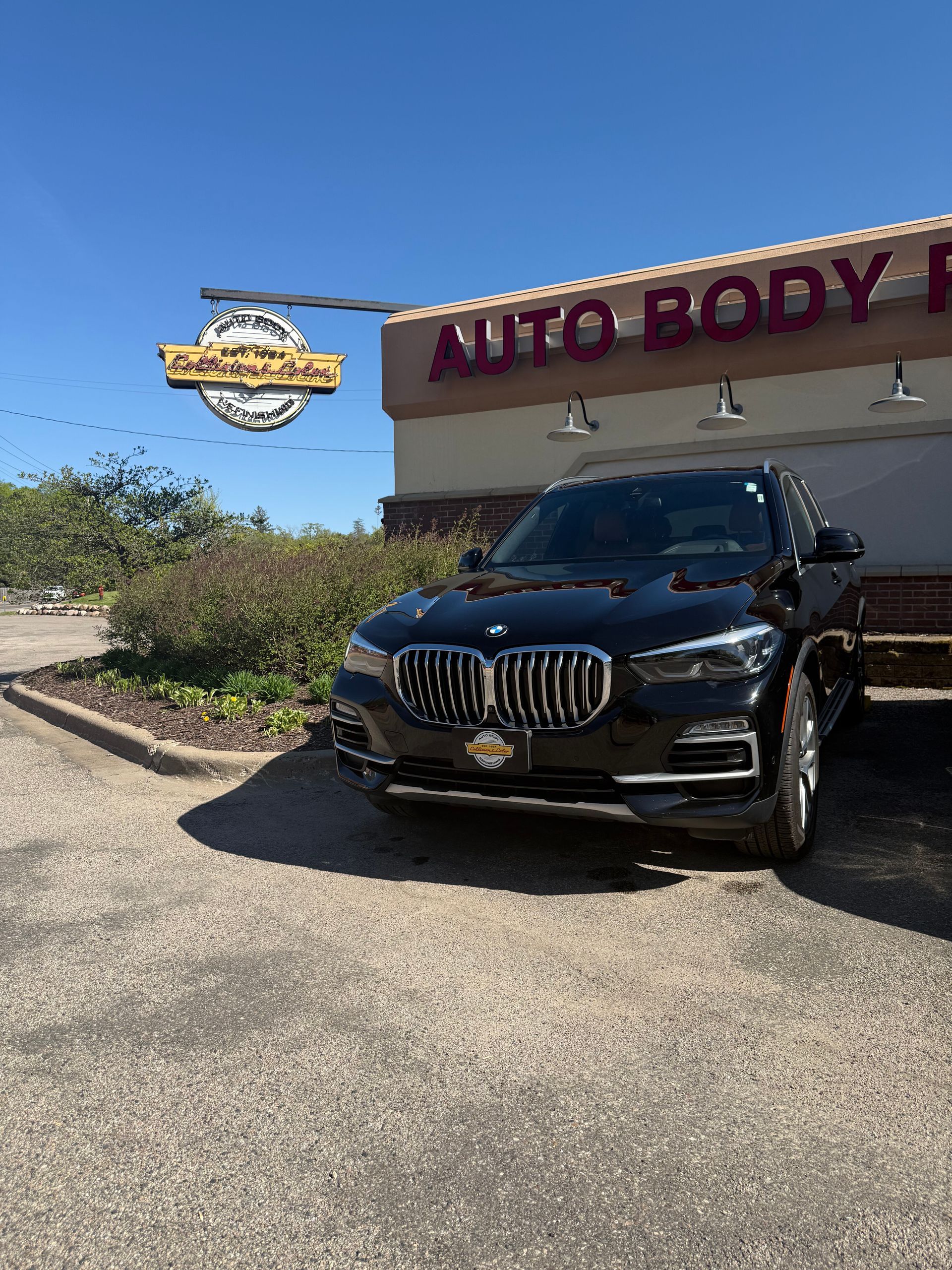 A black BMW is parked in front of an auto body shop