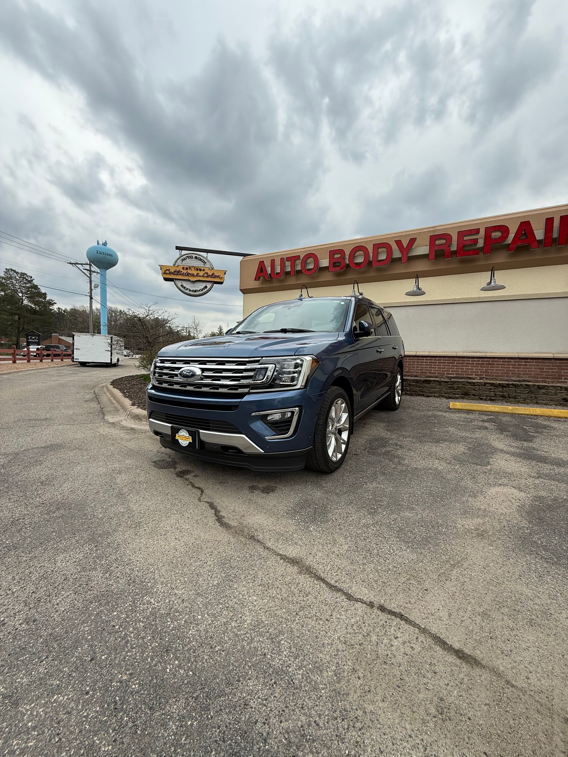 A blue Ford explorer is parked in front of an auto body repair shop