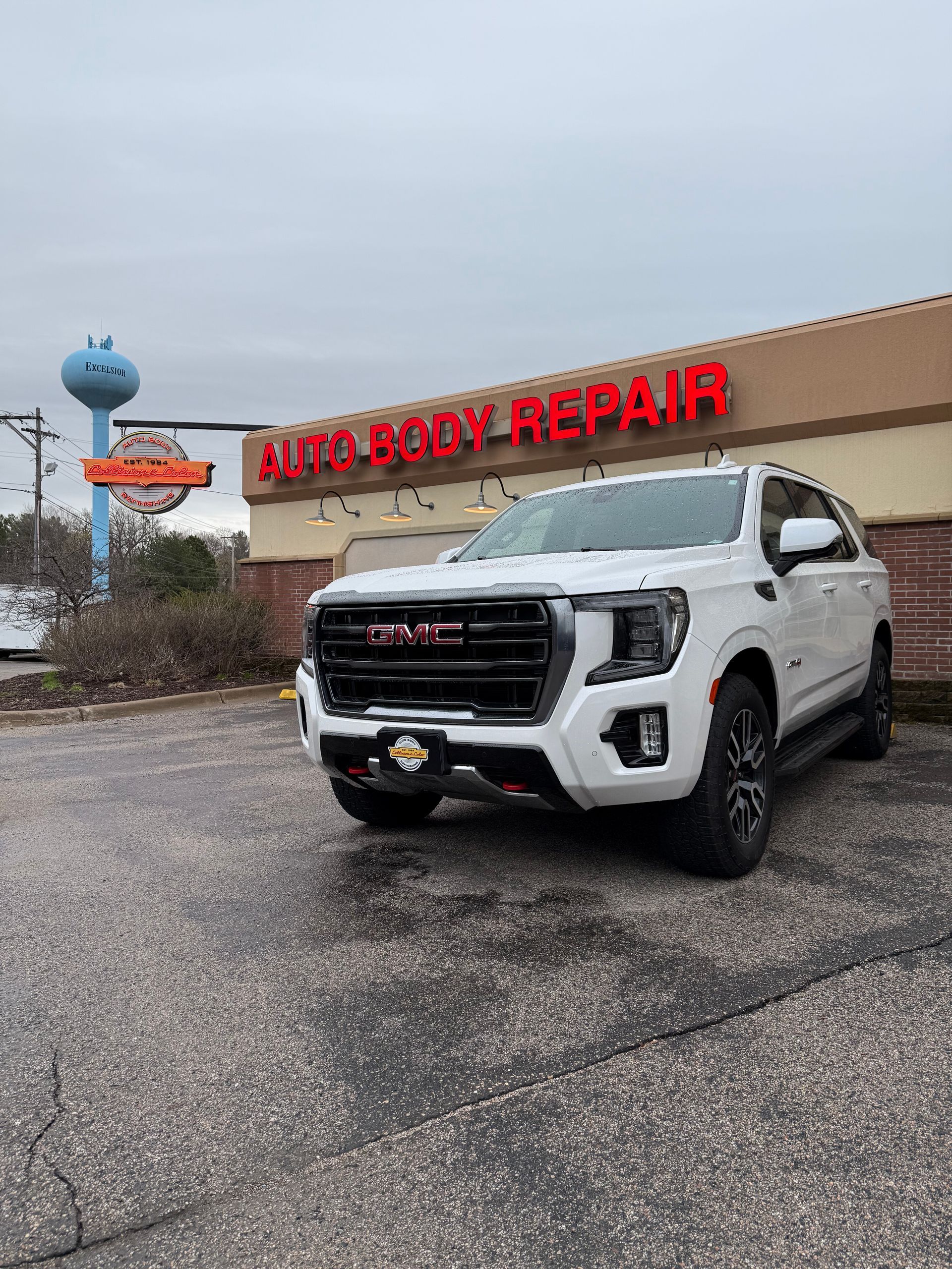 A white GMC truck is parked in front of an auto body repair shop