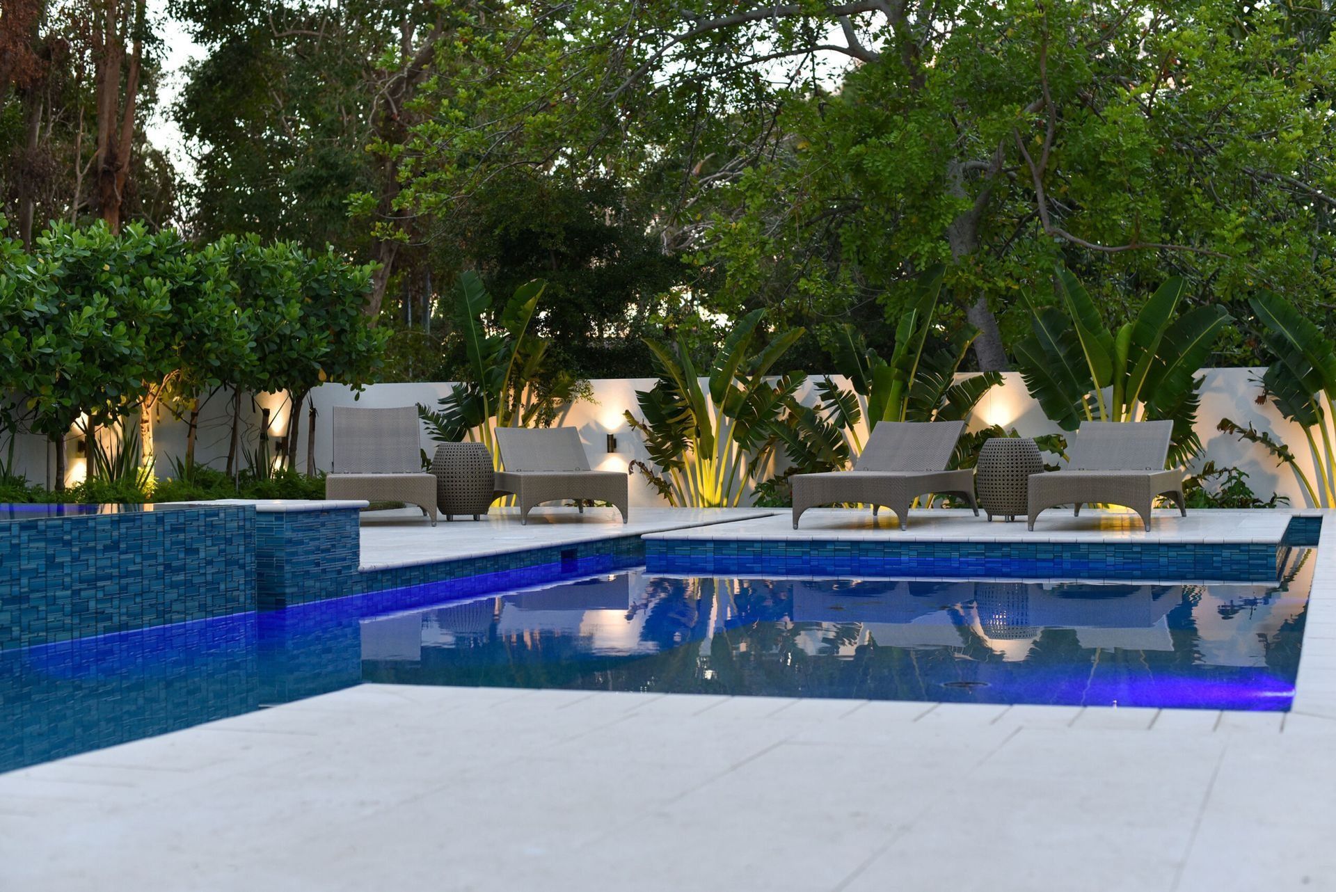 Pool with blue mosaic tile, lounge chairs, and lush greenery.
