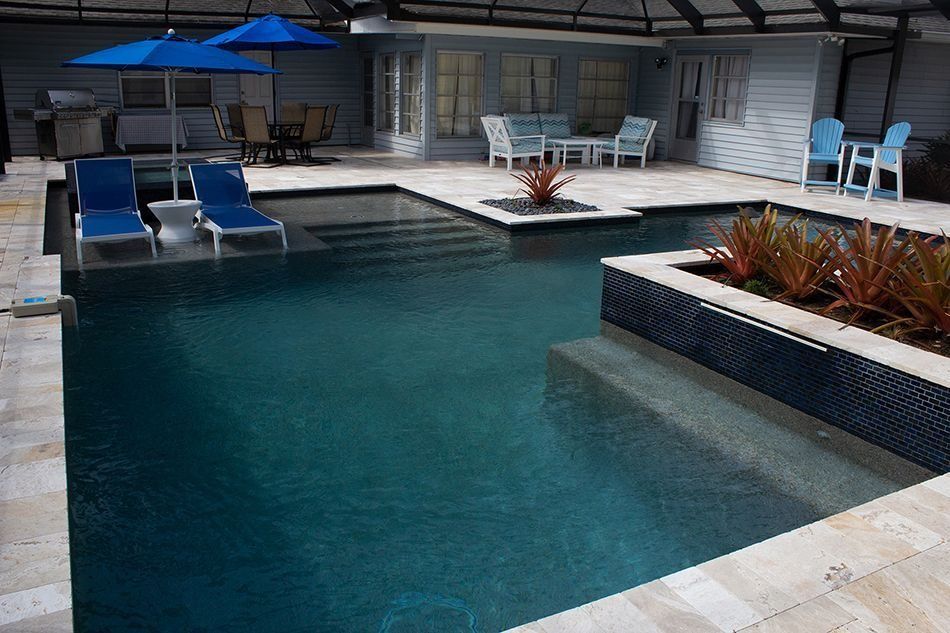 Pool with dark water, lounge chairs, and a seating area with blue accents, in a backyard setting.