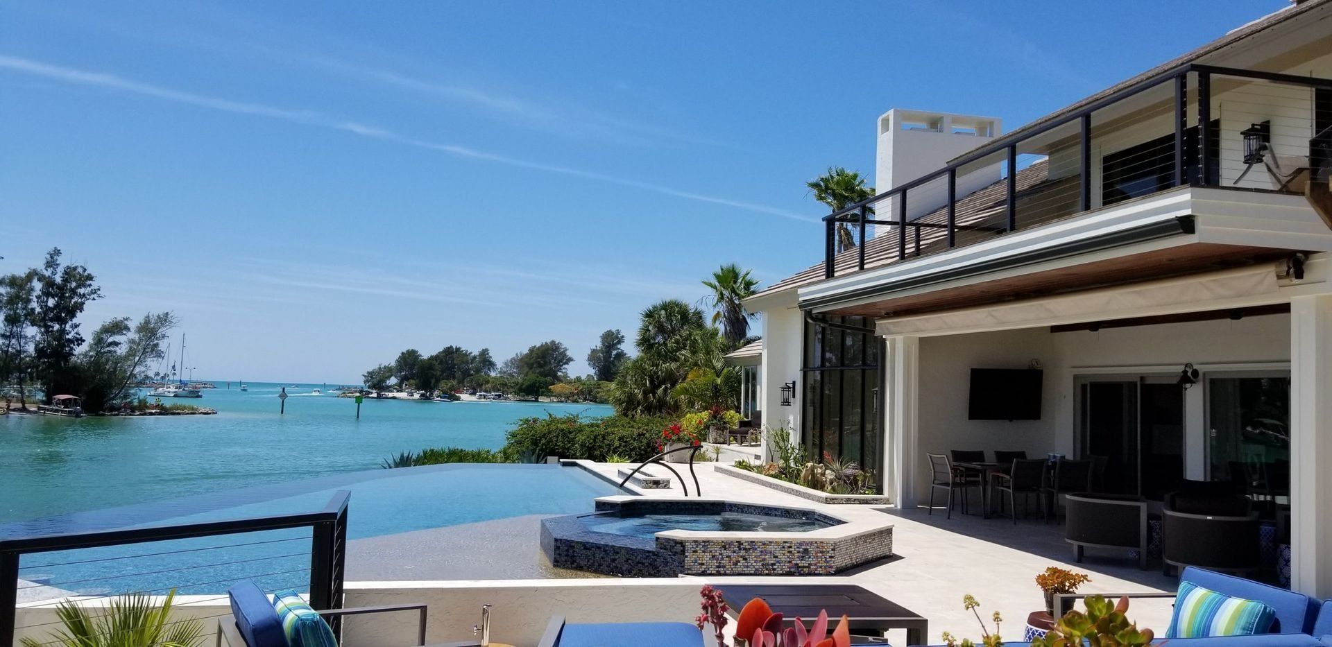 Luxury home with an infinity pool overlooking a body of water under a blue sky.