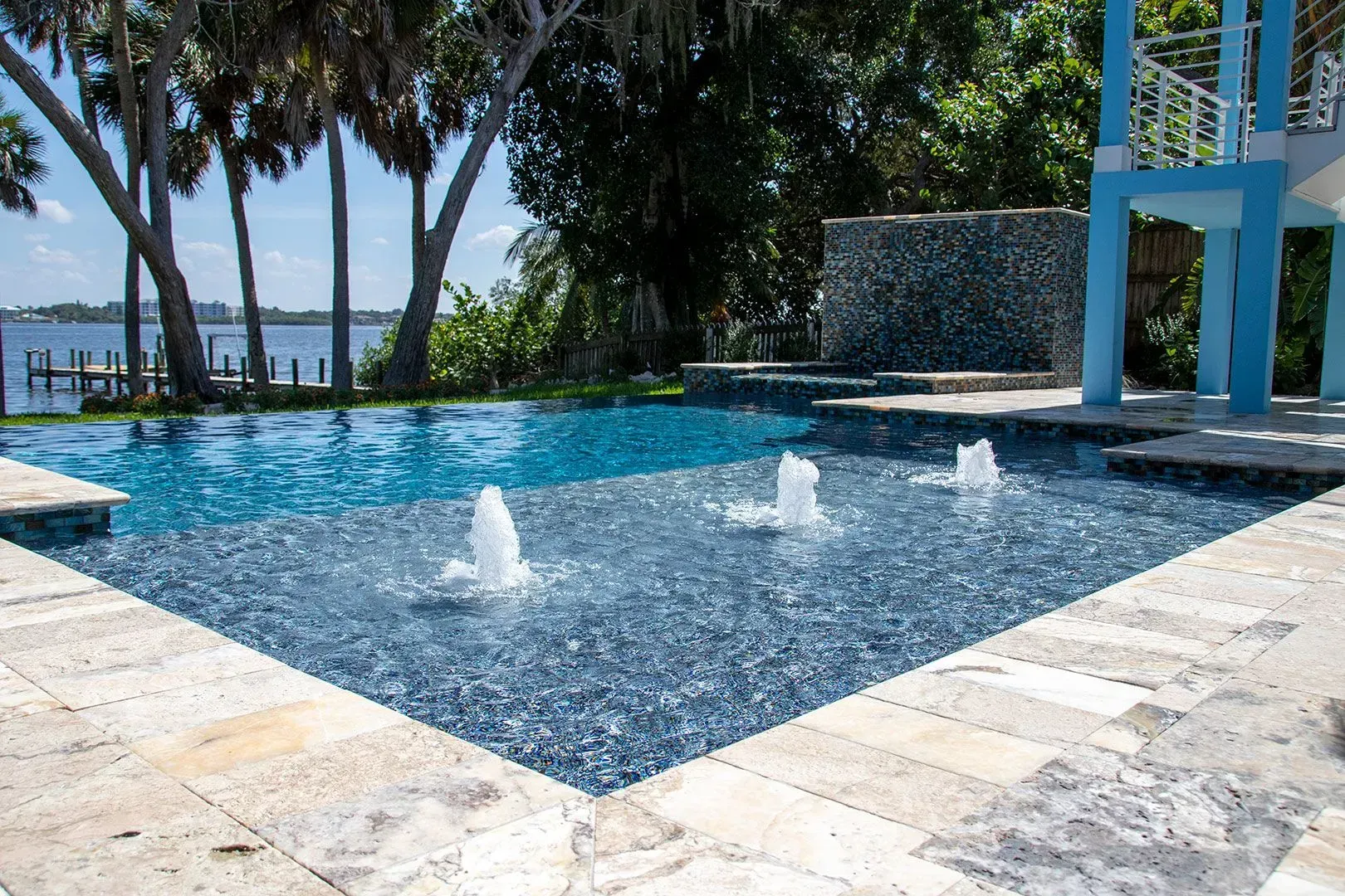 Swimming pool with blue tile, fountains, and stone patio overlooking water.