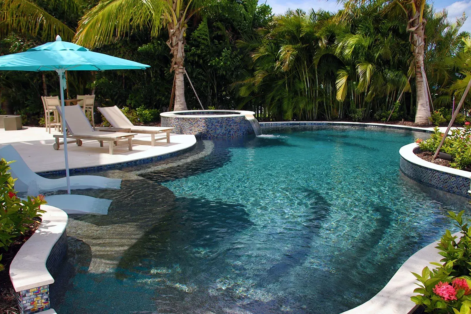 Tropical pool with turquoise water, lounge chairs under an umbrella, and lush greenery.