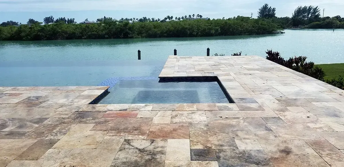 Pool overlooking a bay with green trees in the background and light-colored stone pavers surrounding it.