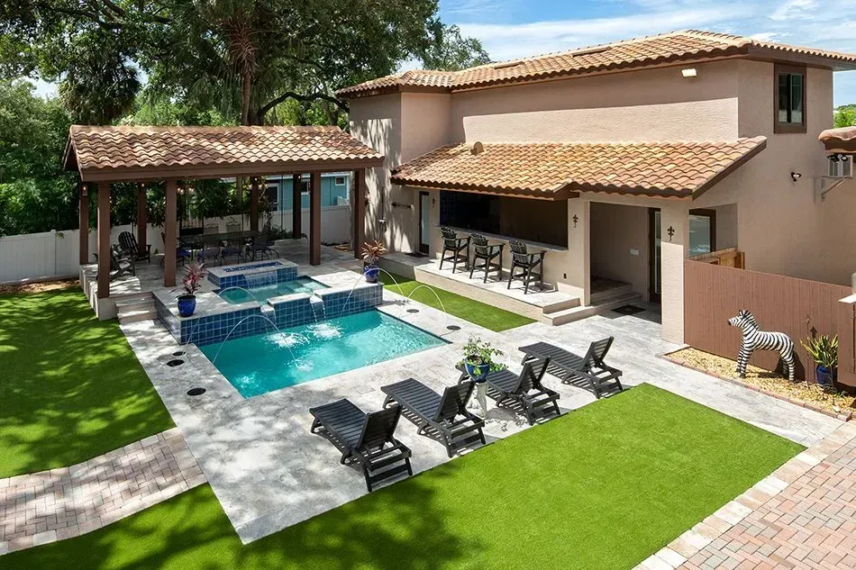 Outdoor area with pool, seating, and a covered bar, with a tan stucco house.