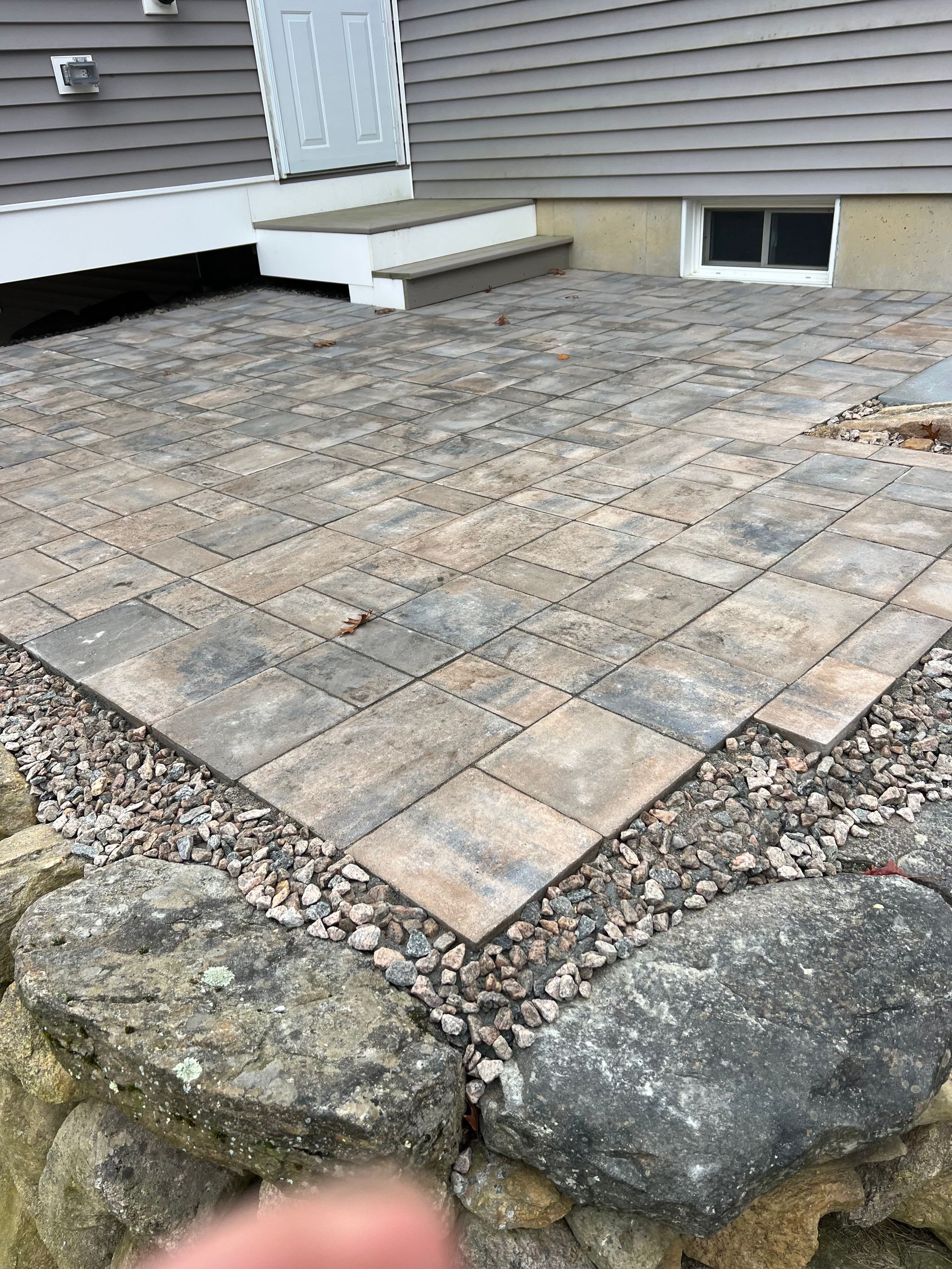 A patio with a stone wall and steps in front of a house.