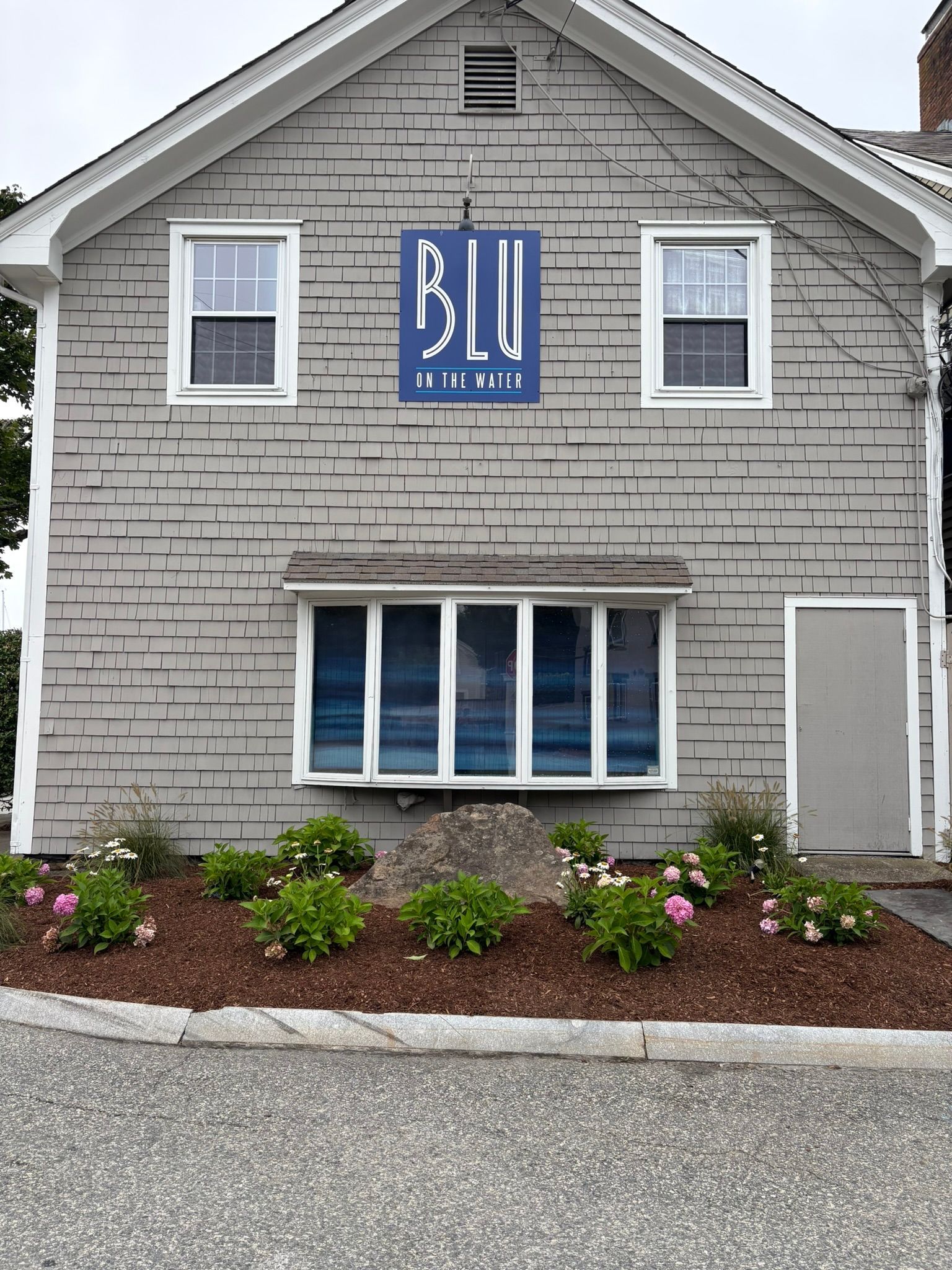 Blu Hair Spa exterior with blue sign, gray building, and floral landscaping.